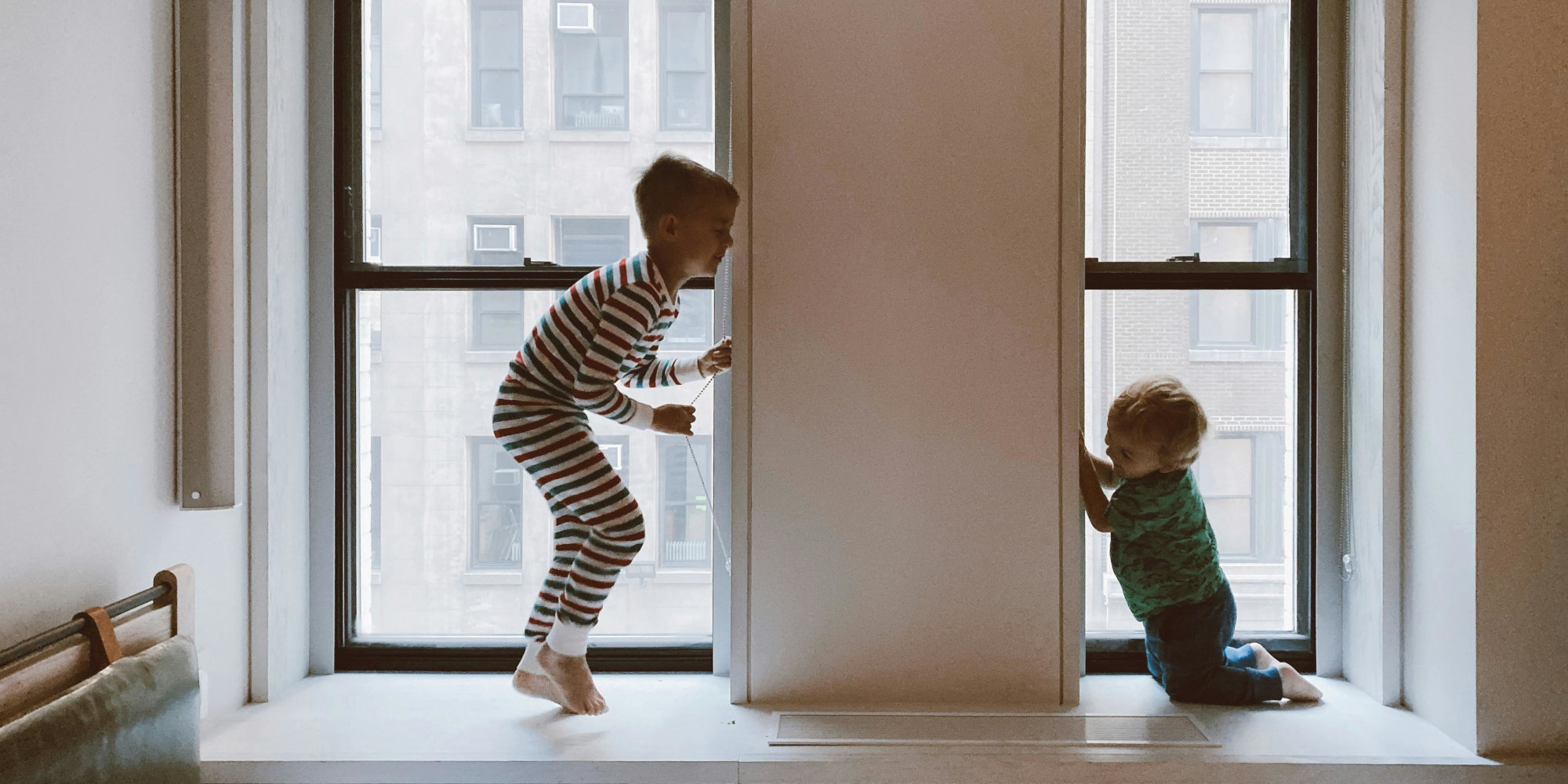 2 children playing in the window sill of a condominium.